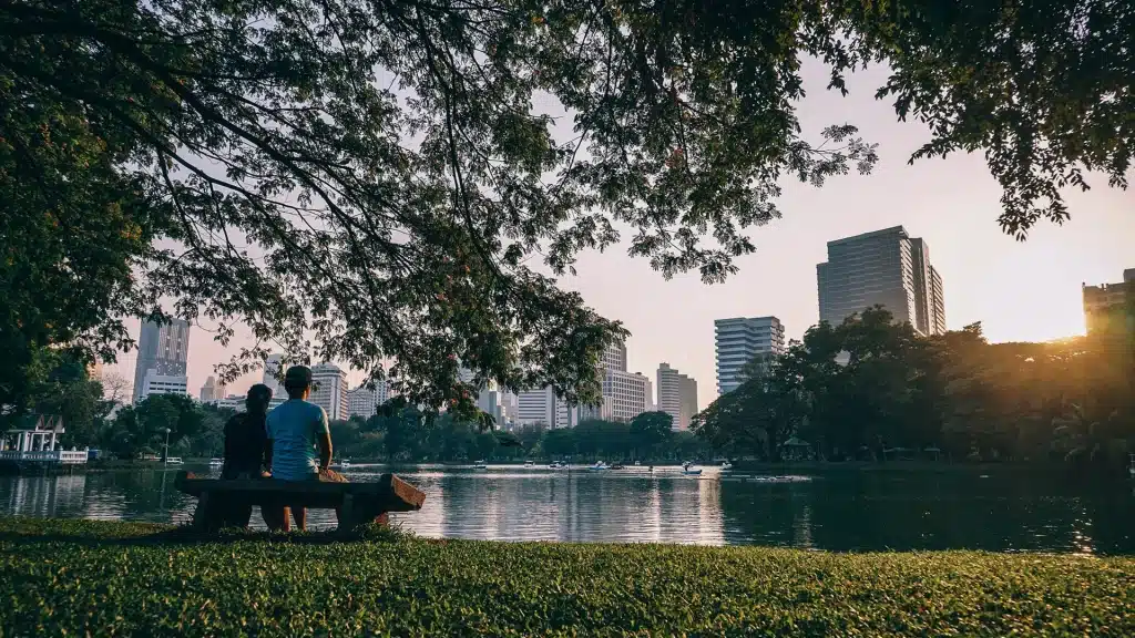 Zwei Personen sitzen auf einer Bank vor einem See in einem park mit Blick auf die Wolkenkratzer